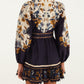 Back view of the Farm Rio Golden Nature Belted Mini Dress, featuring long puff sleeves, a belted waist, and a cream and navy blue floral pattern.