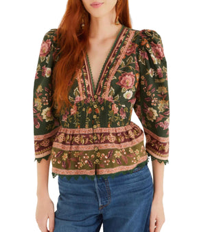 A woman wears the Farm Rio Flowering Garden Tree Green Blouse, featuring floral patterns, puffed 3/4 sleeves, and a deep V neckline, paired with blue jeans.