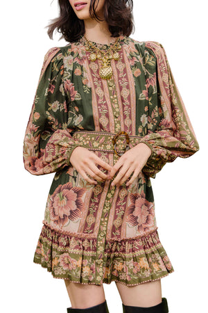 A woman wears the Farm Rio Flowering Garden Tree Green Mini Dress, featuring green florals, long puff sleeves, and pink and beige stripes, styled with a gold necklace and belt—the ideal chic look for a garden party.