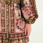Close-up of the Flowering Garden Tree Green Mini Dress by Farm Rio, featuring floral and geometric patterns in pink, green, and brown, a belted waist with round buckle, and a ruffled hem.