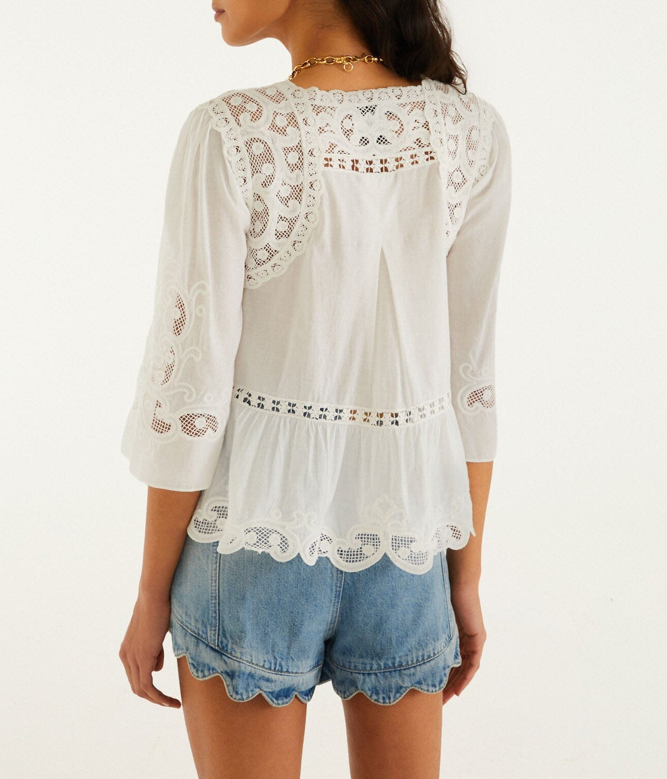A woman is seen from the back wearing a white lace-detailed three-quarter sleeve blouse and Farm Rio’s Light Denim Romantic Wavy Hem Shorts.