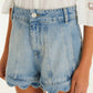 A person wearing Farm Rio Light Denim Romantic Wavy Hem Shorts and a white blouse with embroidered sleeves.