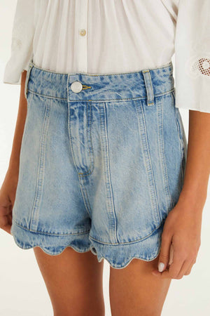 A person wearing Farm Rio Light Denim Romantic Wavy Hem Shorts and a white blouse with embroidered sleeves.