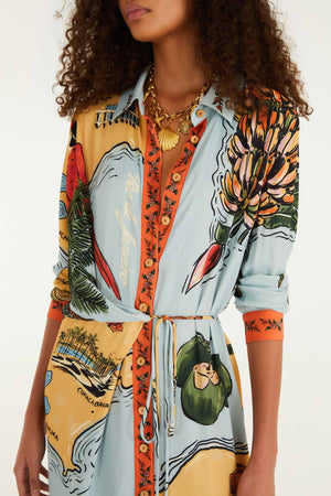 A woman wears the Farm Rio Beaches Path Multicolor Maxi Dress, adorned with vibrant map and botanical prints. She accessorizes with a chunky gold necklace and a shell pendant, her face partially out of frame to emphasize the dress’s striking tropical pattern.
