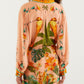 A woman faces away, wearing a peach dress and the FARM Rio Birds Canto Dos Passardos Skirt—a vibrant mini skirt with tropical yellow, green, and orange prints inspired by colorful birds.