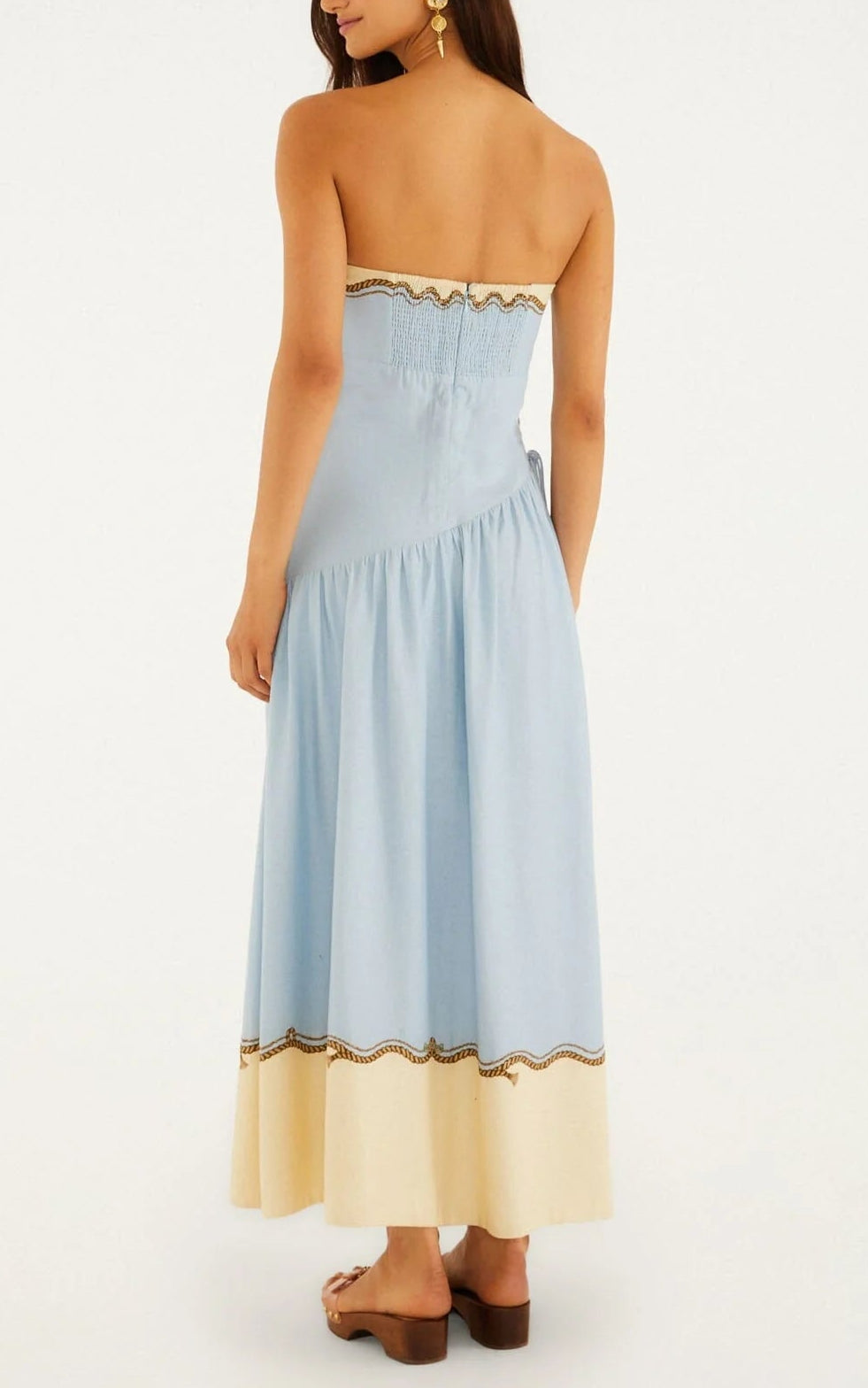 A woman stands with her back to the camera, radiating resort elegance in the Farm Rio Rio Souvenir Mixed Scarf Multicolor Maxi Dress, styled with brown platform sandals and gold earrings against a plain background.
