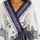A woman wears the Farm Rio Coast Scarf Off White Mini Dress, featuring navy sea-inspired patterns with starfish and shells, plus a matching waist tie.