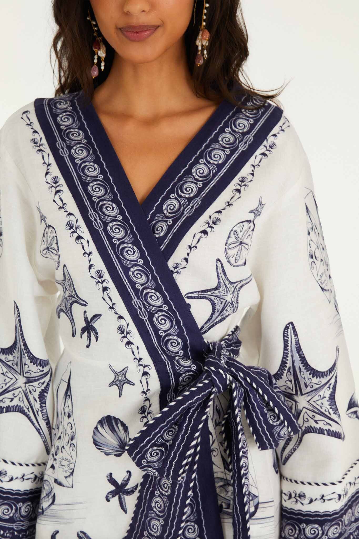 A woman wears the Farm Rio Coast Scarf Off White Mini Dress, featuring navy sea-inspired patterns with starfish and shells, plus a matching waist tie.