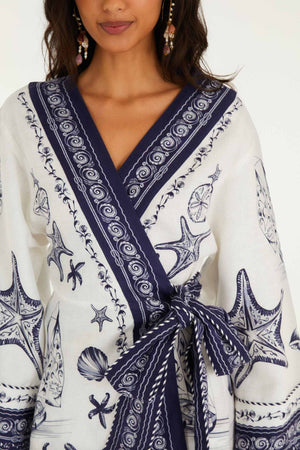 A woman wears the Farm Rio Coast Scarf Off White Mini Dress, featuring navy sea-inspired patterns with starfish and shells, plus a matching waist tie.