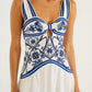 A woman wears the Wonderful City Mix Off White Maxi Dress by Farm Rio, featuring blue floral and geometric patterns, a front knot, and a bust cutout.
