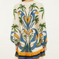 A woman faces away wearing the Farm Rio Tropical Graphic Mini Dress, featuring a cream base with vibrant green, blue, orange, and yellow accents, long sleeves, and a playful ruffled hem.