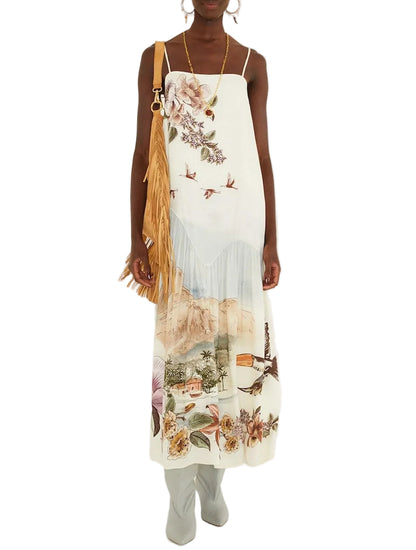Farm Rio Toile De Rio Off White Maxi Dress featuring a landscape print of buildings, trees, birds, and flowers, styled with a tan fringed shoulder bag and grey boots.