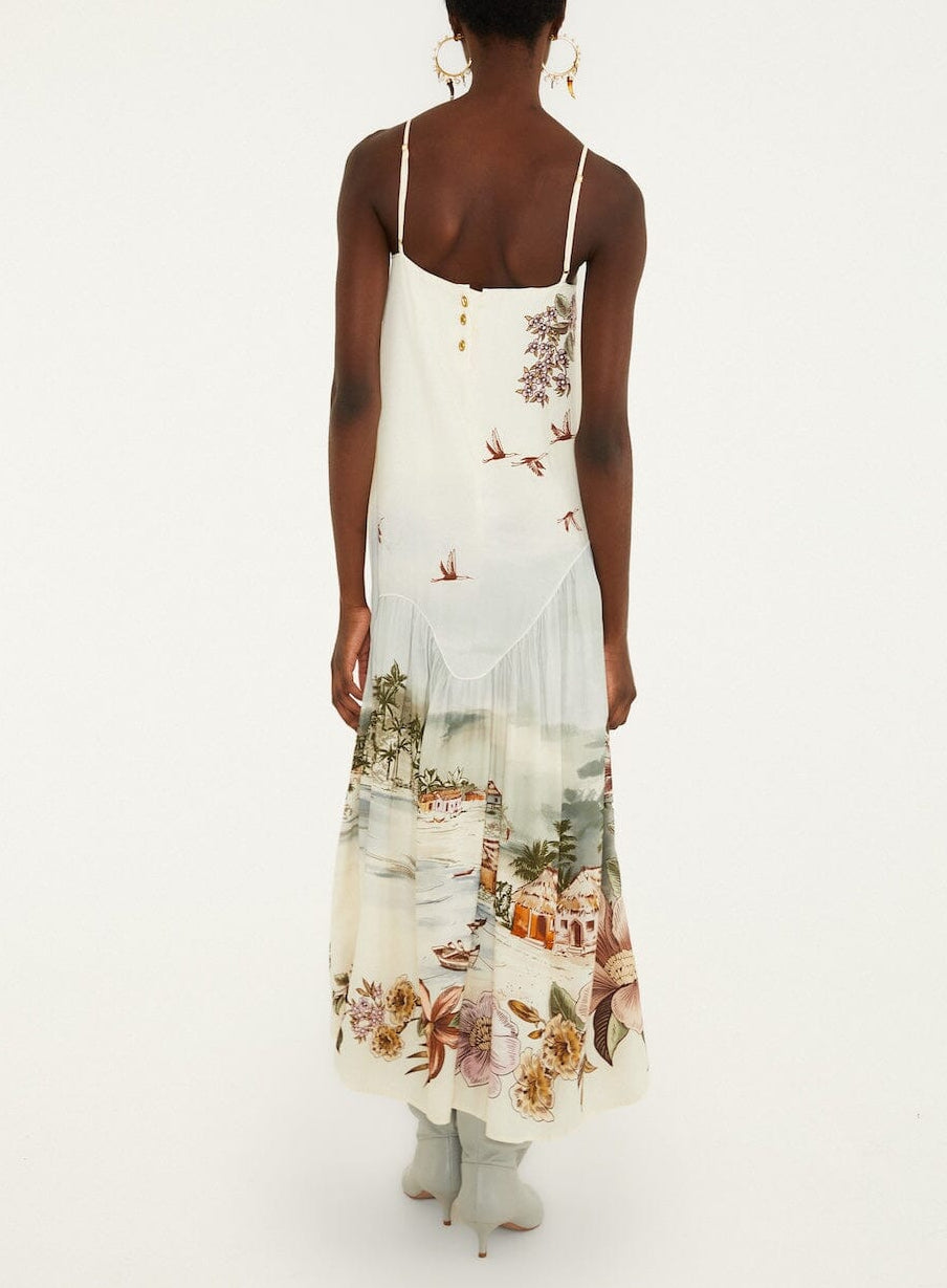 Back view of a person wearing a Farm Rio Toile De Rio Off White Maxi Dress with a tropical landscape and floral print, paired with pale blue heeled boots.