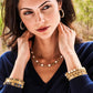 Woman wears navy V-neck sweater and Juliska Capucine De Wulf Berry Gem Medium Hoop Earrings, paired with a gold and pearl necklace plus layered gemstone bracelets—showcasing elegant, feminine jewelry while looking to the side.
