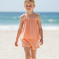 A young girl wearing Feather 4 Arrow’s Girls’ Salty Short with an elastic waistband and a peach-colored sleeveless top walks along a sandy beach with the ocean in the background.