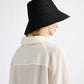 A person wearing a sheer, cream-colored shirt and the Felix Hat by Janessa Leone, a wide-brimmed black summer hat, shown from the back and side.