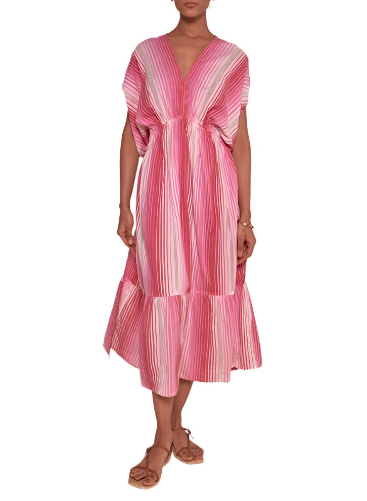 A person wearing the Lemlem Leila Plunge Dress, featuring a pink and white striped pattern, V-neckline, loose sleeves, and a tiered skirt made from 100% cotton hand-woven in Ethiopia, paired with flat sandals.