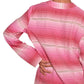 A person with their hand on their hip, wearing a long-sleeve pink lemlem Raey Dress by Lemlem featuring horizontal stripes, is shown from the back. The dress's design subtly resembles the intricate patterns found in garments hand-woven in Ethiopia.