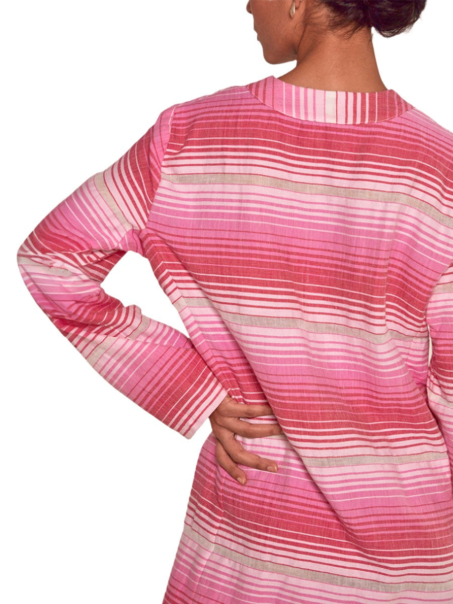 A person with their hand on their hip, wearing a long-sleeve pink lemlem Raey Dress by Lemlem featuring horizontal stripes, is shown from the back. The dress's design subtly resembles the intricate patterns found in garments hand-woven in Ethiopia.