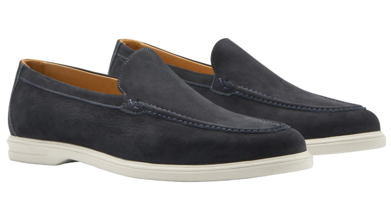 The Peter Millar Excursionist Nubuck Venetian Loafer in dark blue features water-resistant nubuck, white rubber soles, and a light brown interior lining, showcased against a white background.