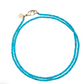 The Jane Win Double Wrap Beaded Necklace is shown on a white background, featuring two strands of turquoise beads in a lariat style with a metal clasp and a small, round tag.