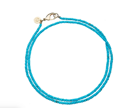 The Jane Win Double Wrap Beaded Necklace is shown on a white background, featuring two strands of turquoise beads in a lariat style with a metal clasp and a small, round tag.