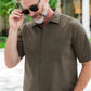 A man with gray hair and beard wears sunglasses and a Herno Seersucker Camp Shirt, standing outdoors with greenery and buildings in the background.