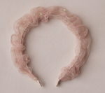 The Noralee Gathered Headband features pink ruffled sheer fabric with small iridescent sequins, perfect for special occasions, shown on a light textured surface.