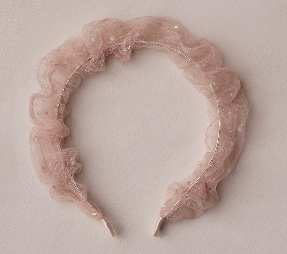 The Noralee Gathered Headband features pink ruffled sheer fabric with small iridescent sequins, perfect for special occasions, shown on a light textured surface.