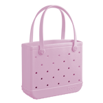 The Baby Bogg Bag by Bogg Bags is a light pink tote with two handles, small side holes, and "bogg" embossed near the bottom. Washable and stylish, it's a practical choice for everyday use.