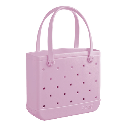 A light pink, rectangular Baby Bogg® Bag tote from Bogg Bags featuring two handles, small round holes on its sides, and “bogg” branding at the bottom corner. This washable and durable bag is ideal for everyday use and provides a customizable tote experience to match your style.