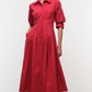 Woman in a Simkhai Jazz Pintuck Midi Dress—long-sleeved, collared, red cotton poplin with an A-line silhouette—standing against a plain white background.