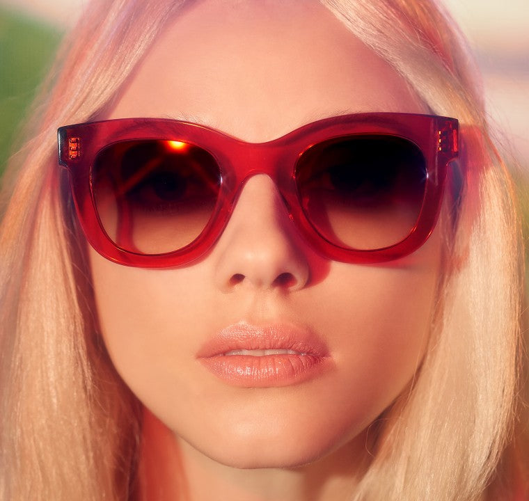 A person with long blond hair wearing large red Thierry Lasry Gambly Sunglasses with a rectangular frame and a neutral expression.