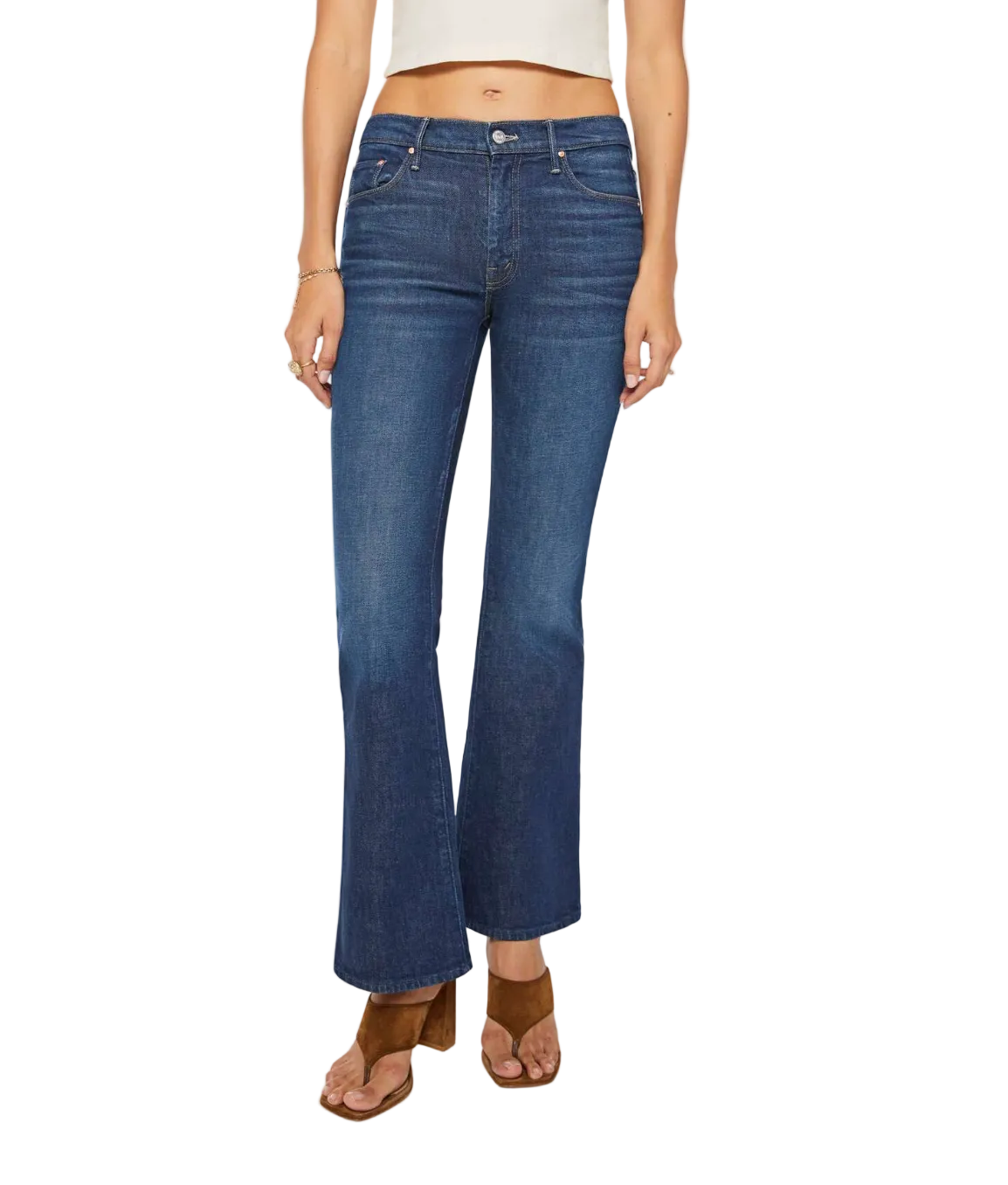 A person wearing The Weekender mid rise blue bootcut jeans by Mother, crafted from stretch denim, paired with a white cropped top and brown heeled sandals, stands against a white background.