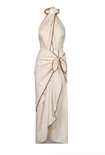 The Centro Del Cielo Ankle Dress by Johanna Ortiz is a sleeveless cream halter-neck dress with brown trim, a draped front, and a side bow at the waist—ideal for intimate gatherings seeking quiet luxury.