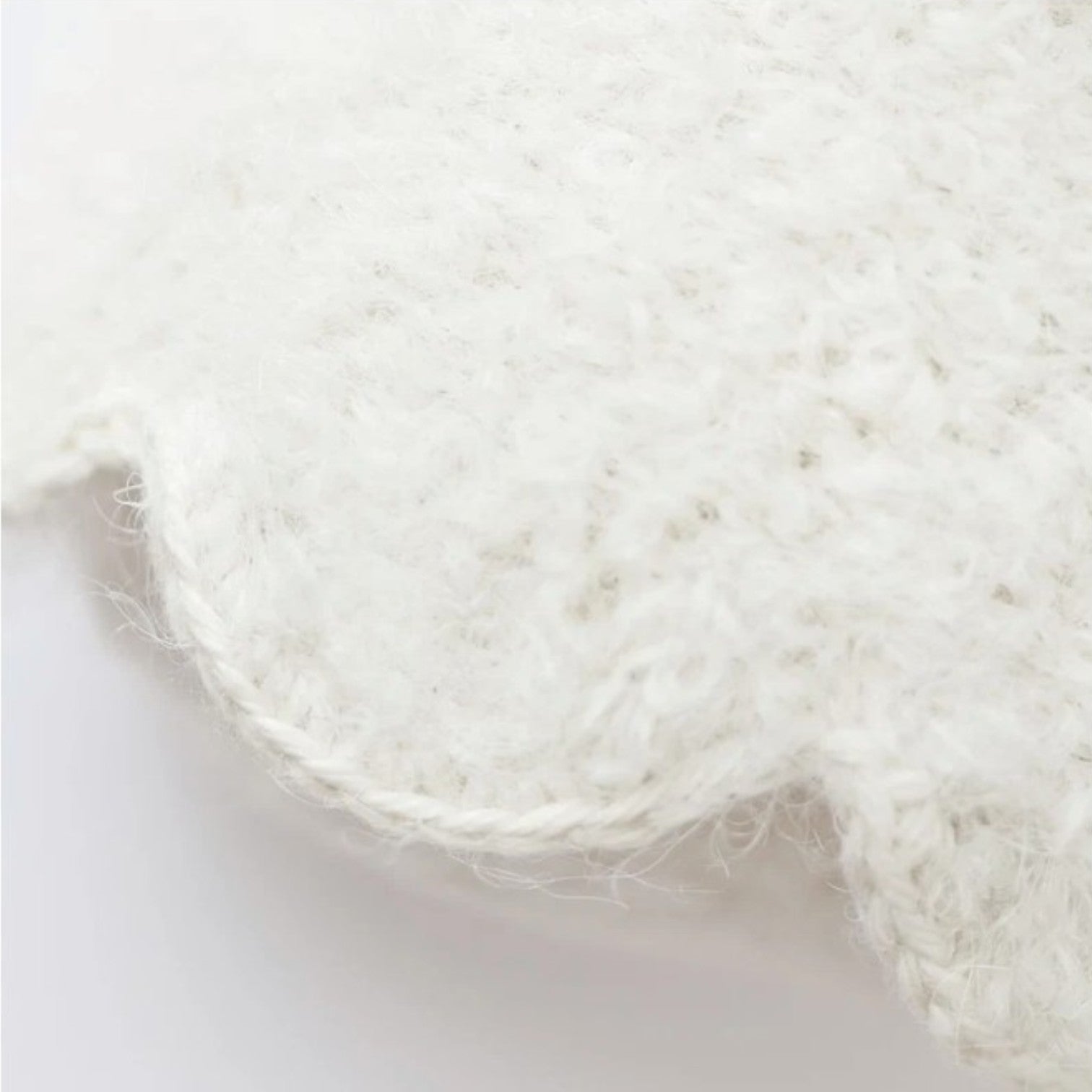 Close-up of Baby Ghost - Pumpkin by Cuddle + Kind, featuring a white, fluffy, scalloped-edge knitted fabric crafted from soft Peruvian cotton yarn against a plain background.