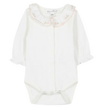 The Tartine et Chocolat Baby Girls’ Ruffled Collar Bodysuit is a white long-sleeve onesie crafted from soft ecru cotton, featuring ruffled cuffs, convenient snap closures, and an embroidered scalloped collar adorned with delicate floral details. This charming bodysuit blends comfort and elegance for a sweet, timeless look.