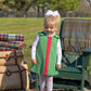 A young girl wears The Beaufort Bonnet Company's Baby and Kids' Tatum's Turtleneck, standing on gravel near baskets, plaid blankets, and a green chair outdoors.