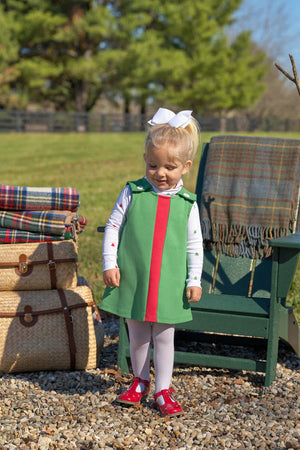 A young girl wears The Beaufort Bonnet Company's Baby and Kids' Tatum's Turtleneck, standing on gravel near baskets, plaid blankets, and a green chair outdoors.