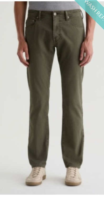Wearing the AG Jeans Everett Slim Straight twill linen pants in olive green with a mid-rise waist, paired with a light grey shirt tucked in and beige sneakers, the person stands against a plain light background.