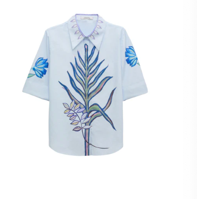 The Floral Embrace Blouse by Dorothee Schumacher is a light blue cotton-poplin short-sleeve blouse with a large botanical key print on the front, blue floral sleeves, and decorative collar details.