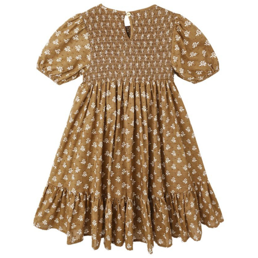The Girls' Lydia Dress by Rylee & Cru is a brown, knee-length smocked dress with short sleeves, a white floral pattern, ruffled hem, and button closure at the back.