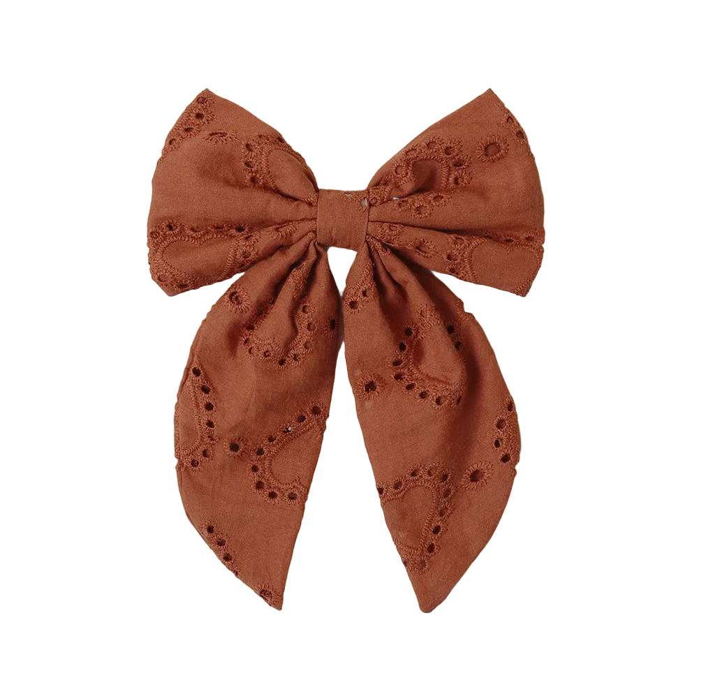 The Noralee Girls' Everly Bow features brown embroidered eyelet details, two long tails, and a rose gold alligator clip—creating a charming hair accessory for girls. Shown on a white background.