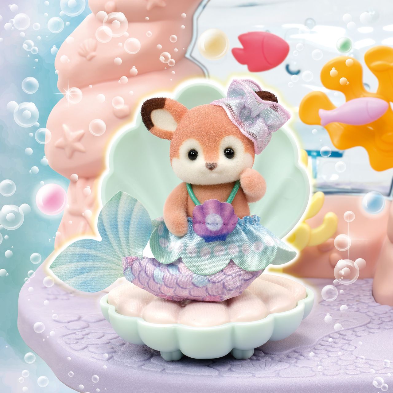 A Calico Critters Baby Mermaid Castle set features a toy fox dressed as a mermaid with a blue tail, sitting in an open shell and surrounded by underwater decorations and bubbles, creating the enchanting scene of an undersea castle adventure.