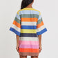 A person stands facing away, wearing the Lemlem Belkis Caftan—a knee-length, hand-woven garment with wide horizontal stripes in blue, orange, green, pink, and yellow.