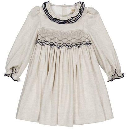 The Kidiwi Baby Girls' and Girls' Hars Organic Cotton Twill Smocked Dress features a cream color, long sleeves, ruffled cuffs, a gathered skirt, and black embroidery on the collar and chest.