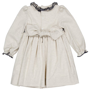 The Kidiwi Baby Girls' and Girls' Hars Organic Cotton Twill Smocked Dress features long sleeves, a beige hue, black ruffle trim on the collar and cuffs, a buttoned back, and a large waist bow.