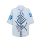 The Floral Embrace Blouse by Dorothee Schumacher is a light blue classic shirt with a botanical key print on the front and blue floral details on the sleeves and collar.