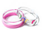 Lillies & Roses Unicorn & Stars Pink Bangles—three overlapping plastic bracelets including one solid pink, one clear, and one clear with pastel rainbow and star decorations—make the perfect sparkling jewelry for unicorn lovers and fun kids accessories.