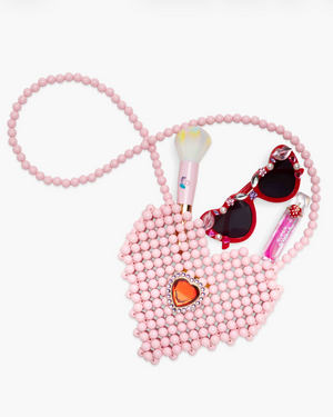 The Super Smalls Heartfelt Sparkle Pearl Handbag, child-sized heart sunglasses, a makeup brush, and pink lip gloss are arranged on a white background.